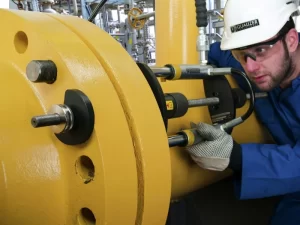Técnico ajustando junta de flange com papelão hidráulico em sistema de tubulação.